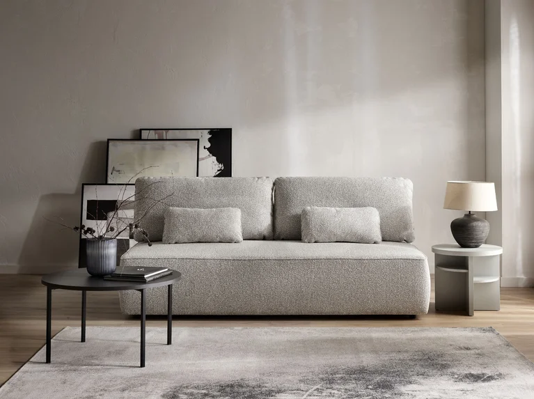 Niewielka szara sofa na tle beżowej ściany